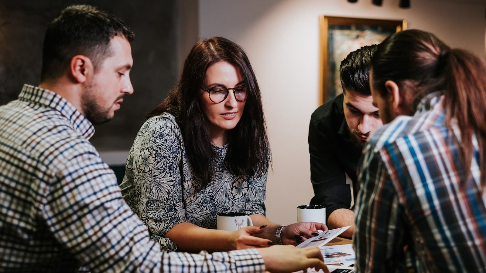Four colleagues leaning over a table, reading through printed documents together.