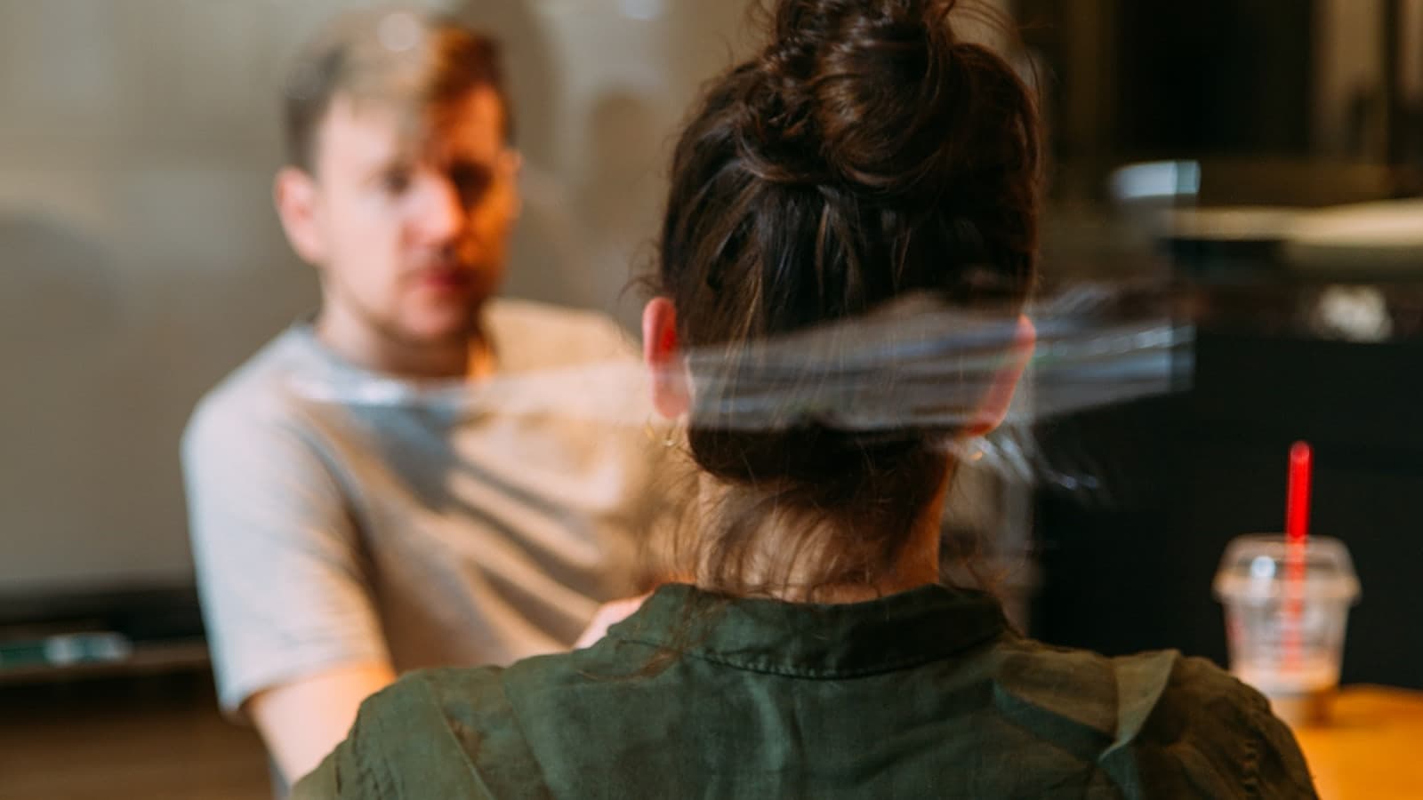 Two people in conversation across a table in a café, seen through the window.
